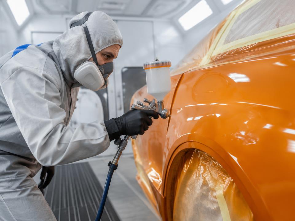 Technician spray painting a car in a paint booth